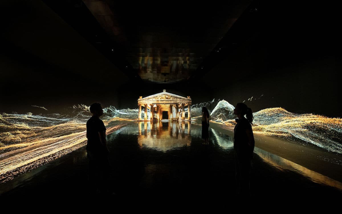 A group of people standing in a dark room with light projected on them - EPHESUS – EXPERIENCE MUSEUM