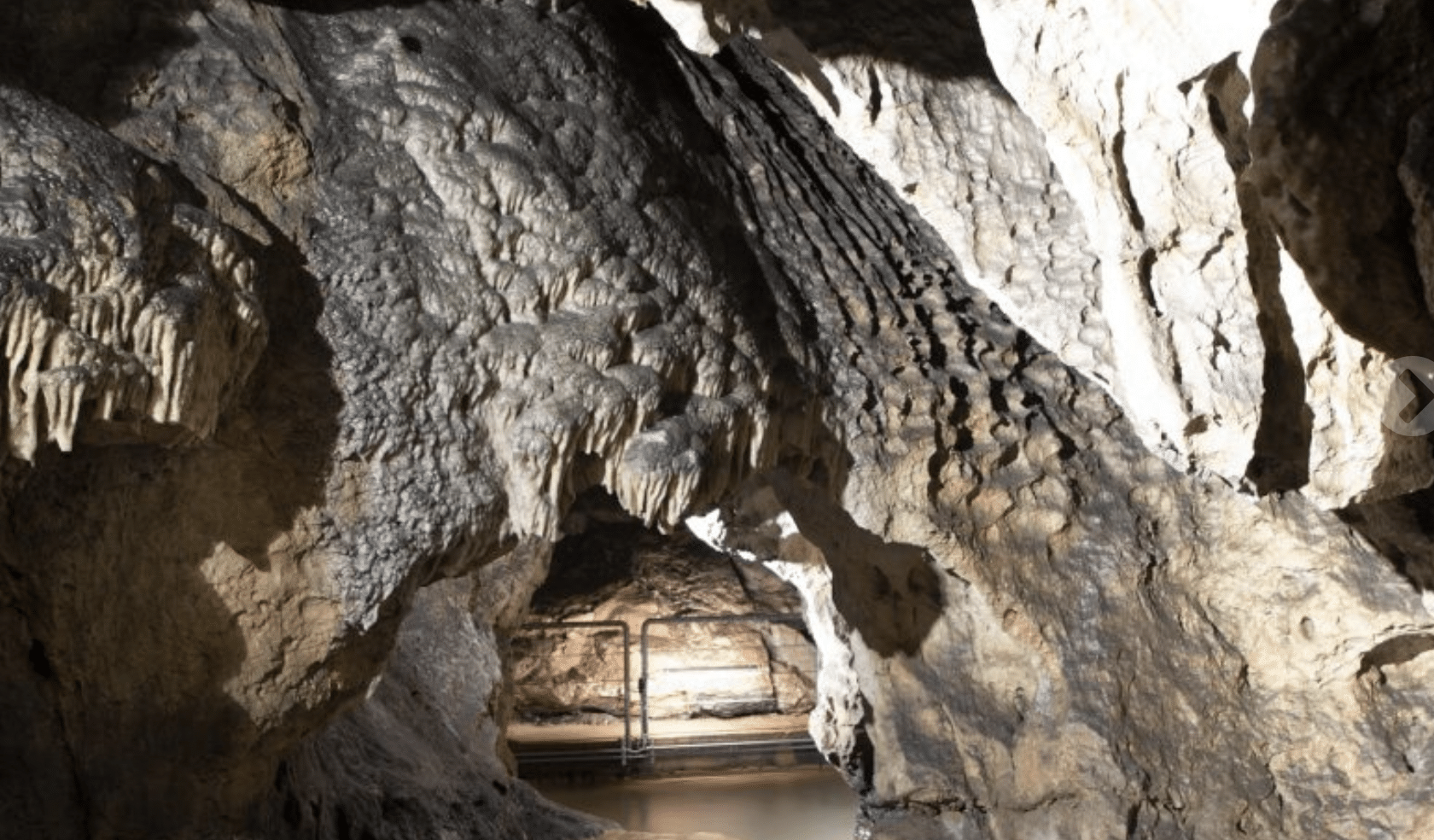 A Slovenian limestone cave interior with stalactites and a walking path illuminated by artificial lighting - Hell Cave (Pekel Cave)